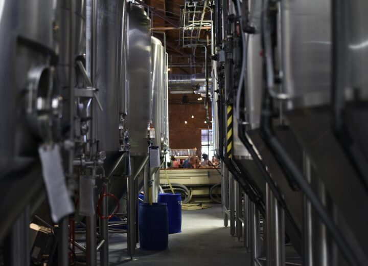 Inside view of a modern brewery with large stainless steel tanks and machinery for beer production.