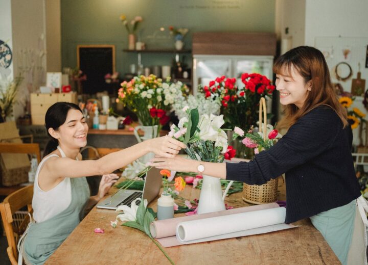 Two smiling women in a floral shop creating beautiful bouquets and arrangements.