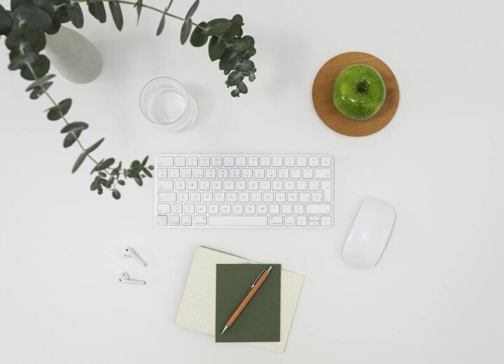 From above of modern wireless devises placed on white table among notebooks and vase with branch of eucalyptus and ripe green apple